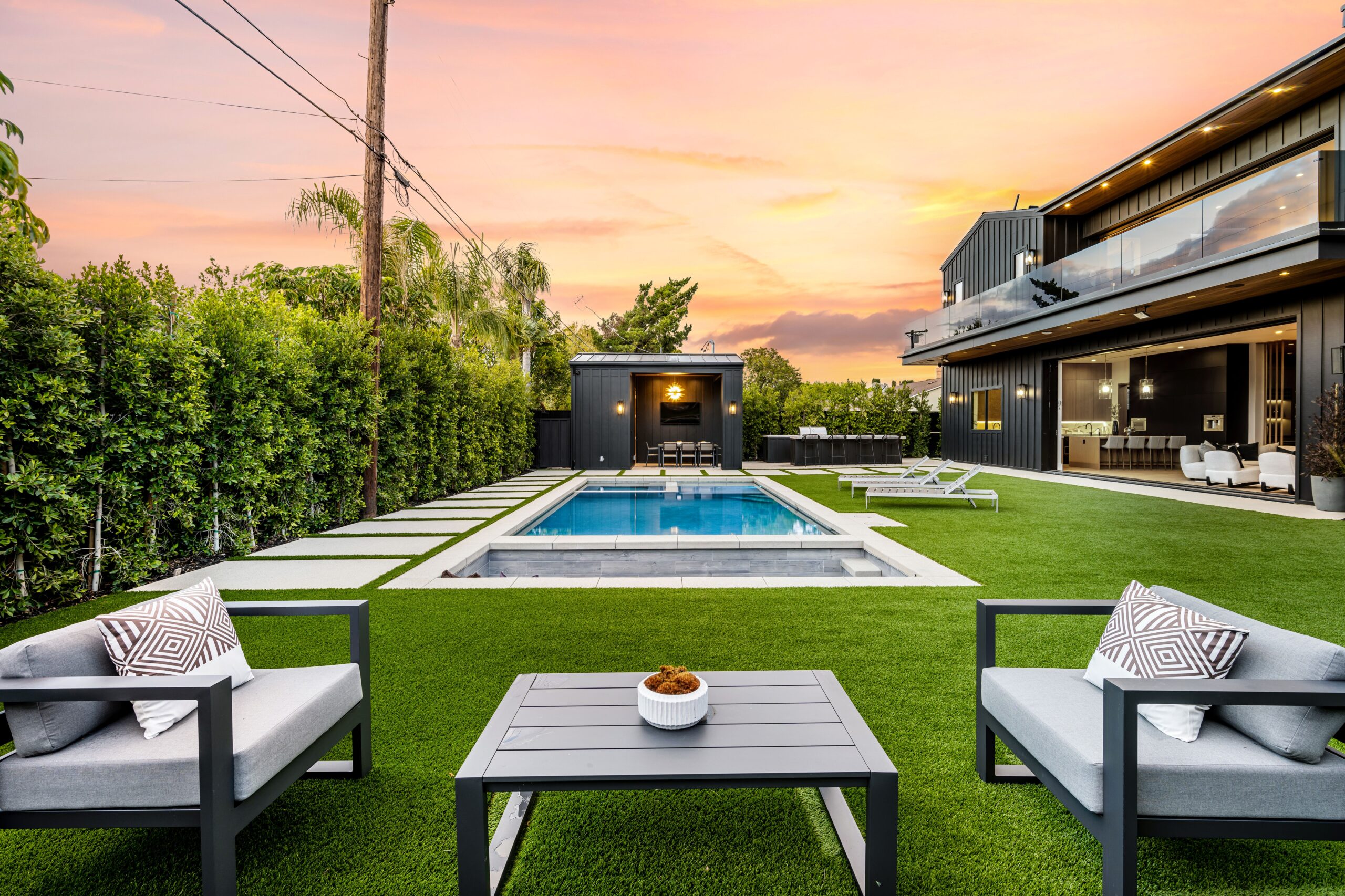 A modern backyard with a swimming pool, seating area, and a contemporary house at sunset.