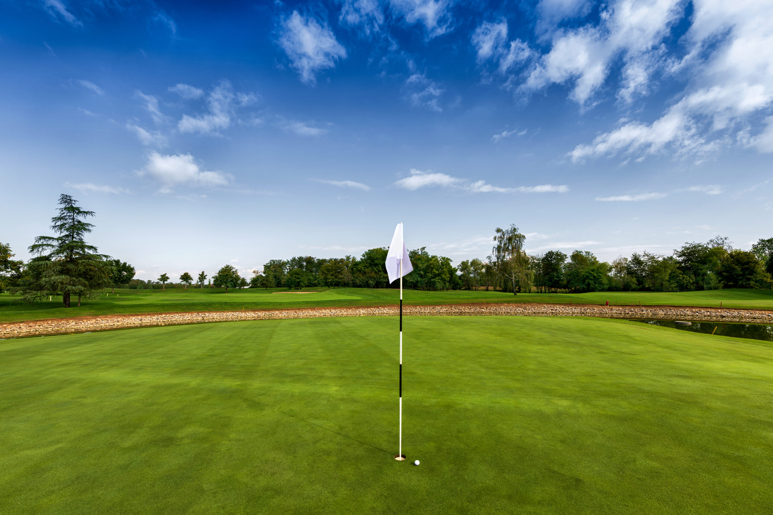 Small ball close to hole with white flag showing position on green grassy field of golf club